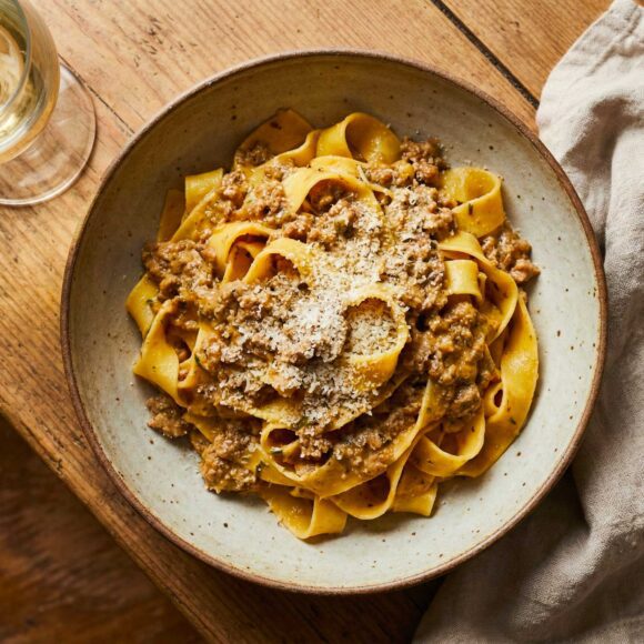 Close up of fresh Tagliatelle al Ragù Bianco in a ceramic bowl topped with cheese.