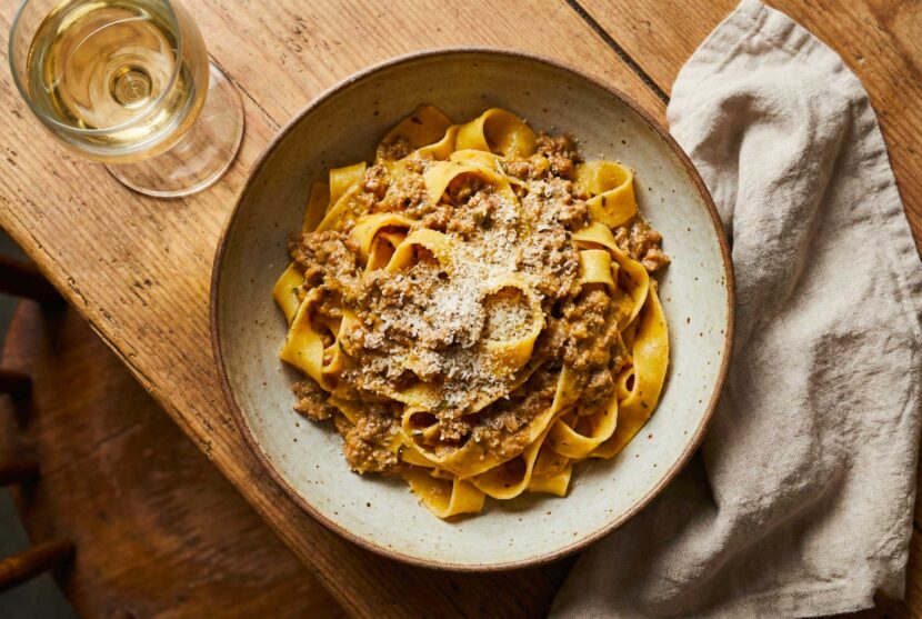 Close up of fresh Tagliatelle al Ragù Bianco in a ceramic bowl topped with cheese.