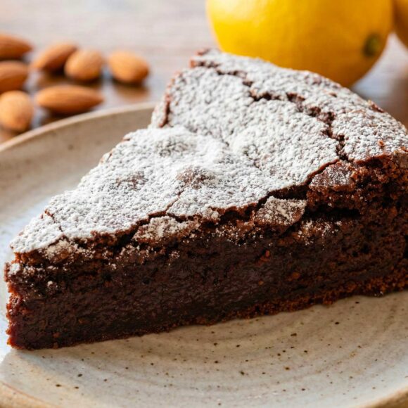 A slice of dark chocolate Torta Caprese on a white plate dusted with powdered sugar.