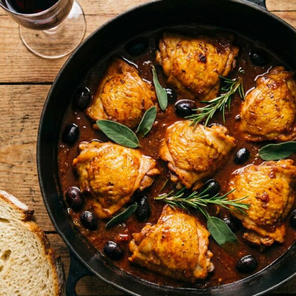 Pollo alla Cacciatora (versione Toscana) in a rustic pot with fresh herbs and olives.