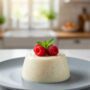 A perfectly unmolded Panna cotta classica on a white plate, garnished with a single mint leaf and three raspberries.
